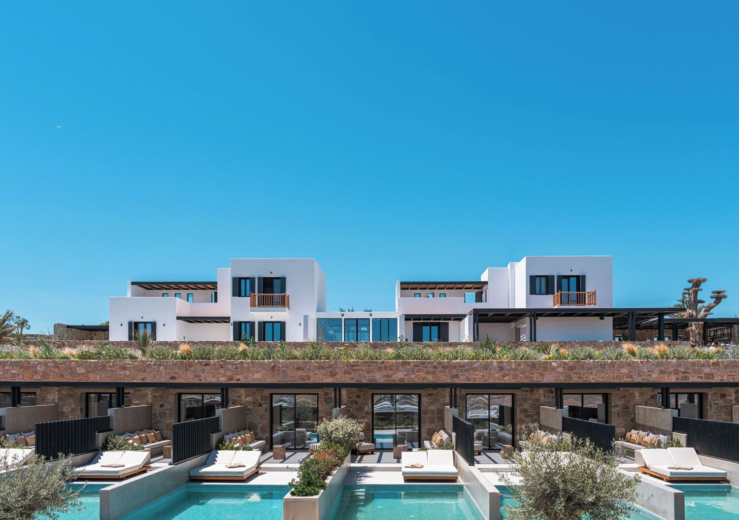 A modern hotel with a pool area, multiple balconies, and a clear blue sky.