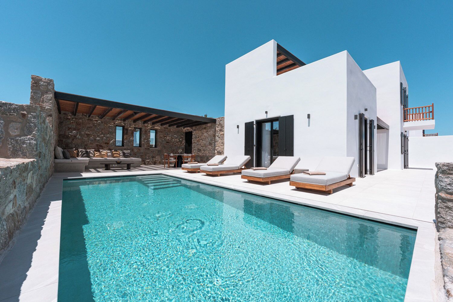 A modern poolside area with a clear pool, lounge chairs, and a stone wall.