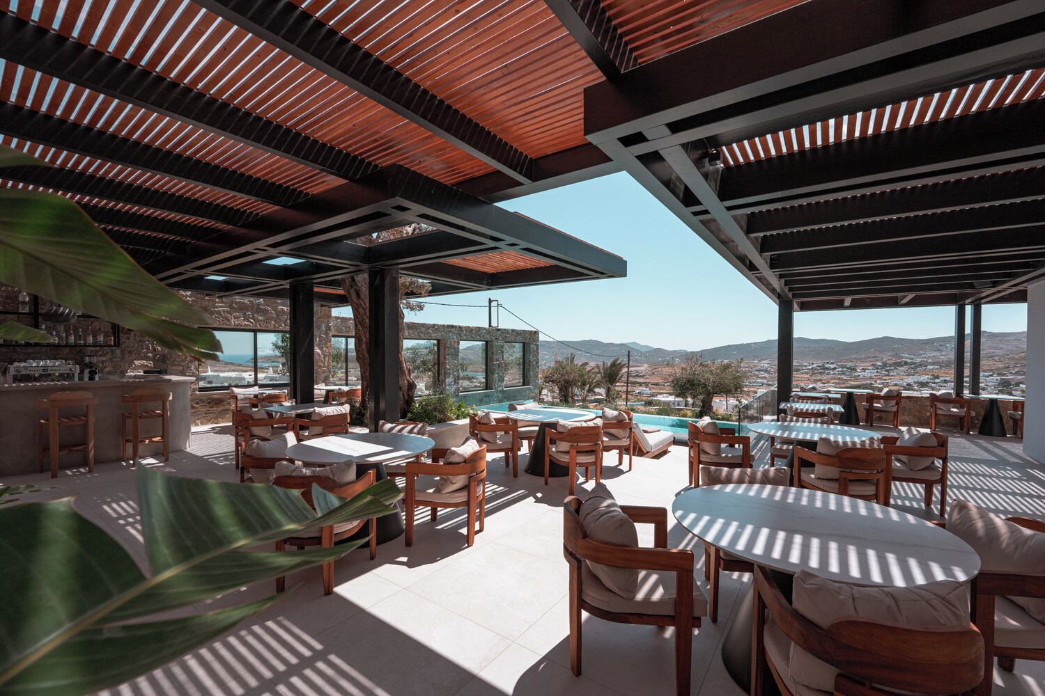 An outdoor seating area with tables and chairs, overlooking a pool and a scenic view of the landscape.