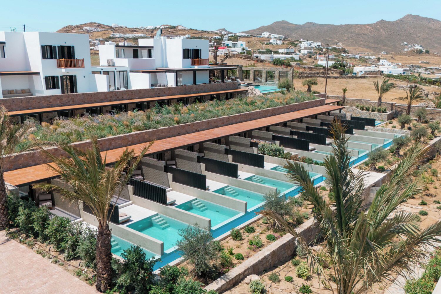 A modern resort with multiple swimming pools, a covered seating area, and a view of the surrounding landscape.