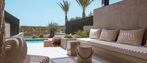 Un área de estar exterior moderna con piscina, muros de piedra y palmeras.