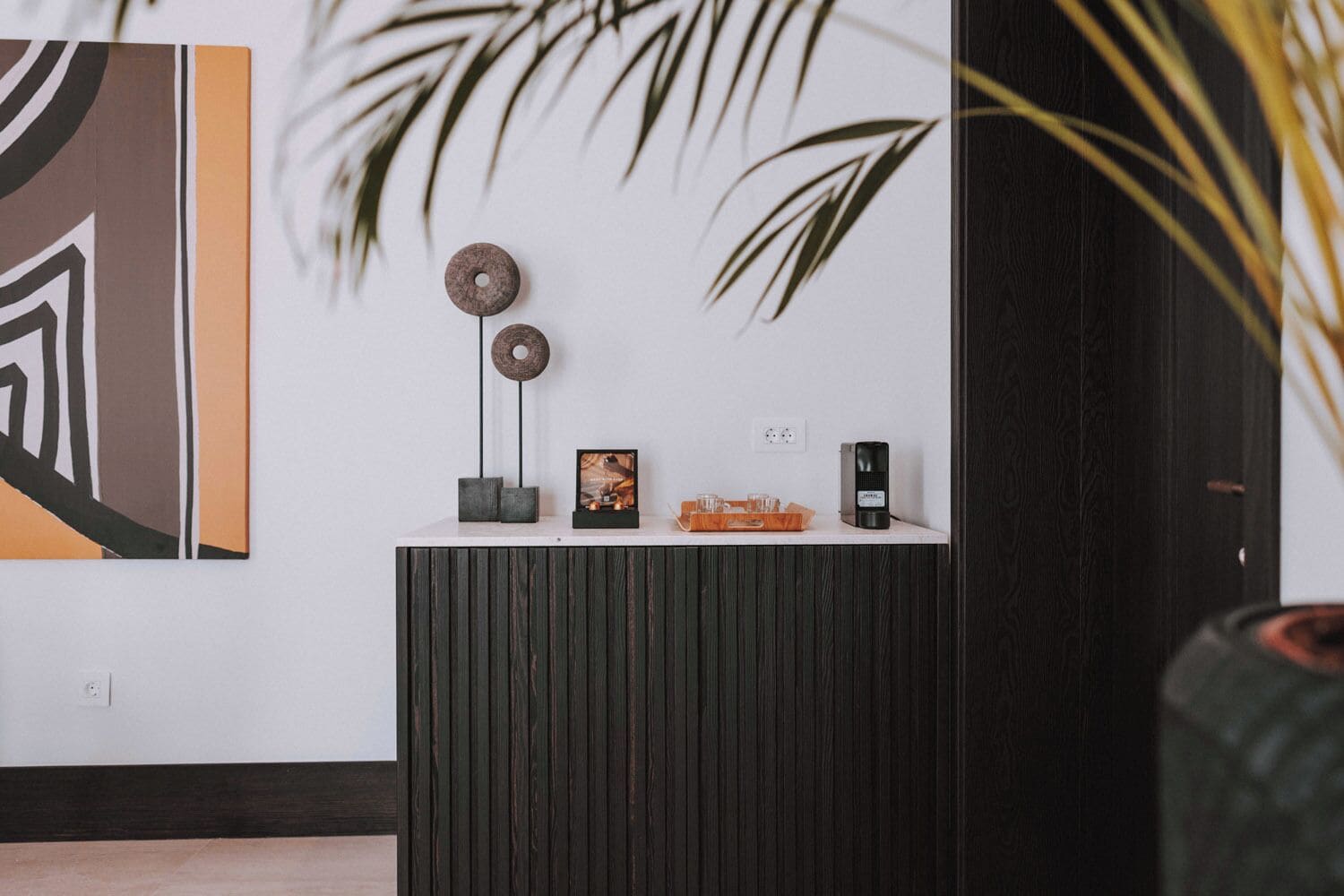 A reception desk with a modern design, featuring a wooden panel, a framed picture, a small plant, and a decorative item.