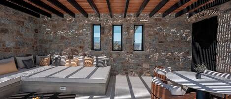 Una habitación de paredes de piedra y techo de madera, con un sofá, una mesa de comedor y dos ventanas con vistas.