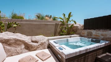 A hot tub with a stone wall backdrop, a lounge area with towels, and a clear blue sky.