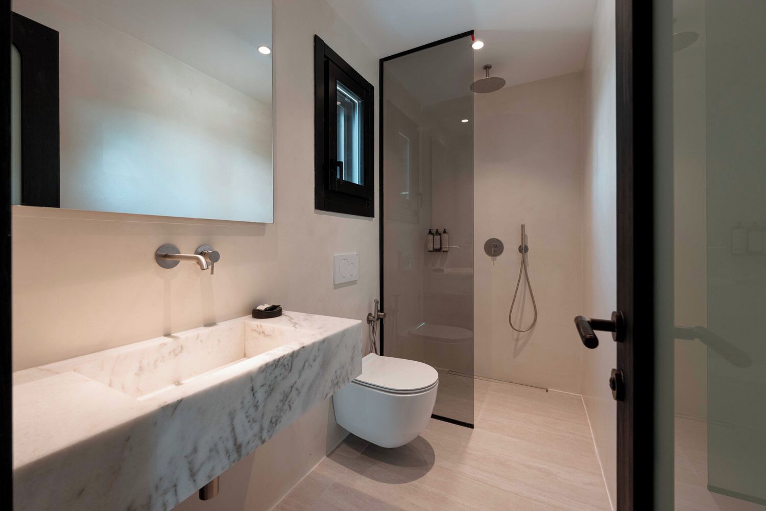 A modern bathroom with a marble sink, toilet, and glass-enclosed shower.