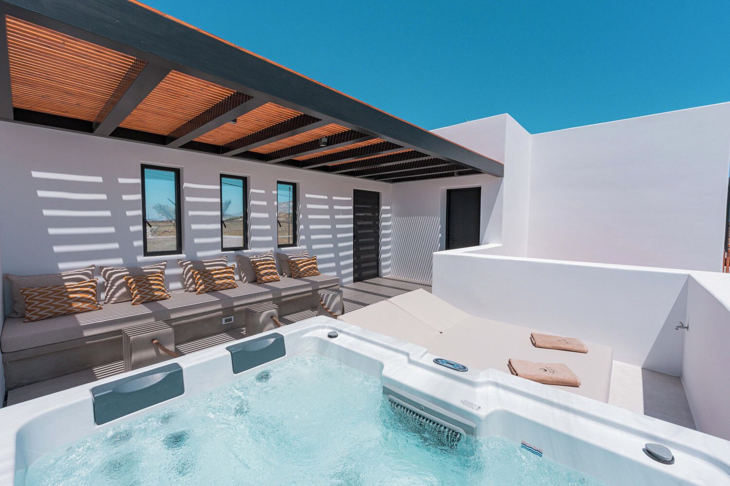 Un área de piscina moderna al aire libre con un jacuzzi, asientos con cojines y una estructura de pérgola.