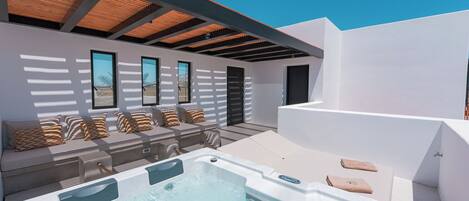 Un área de piscina moderna al aire libre con un jacuzzi, asientos con cojines y una estructura de pérgola.