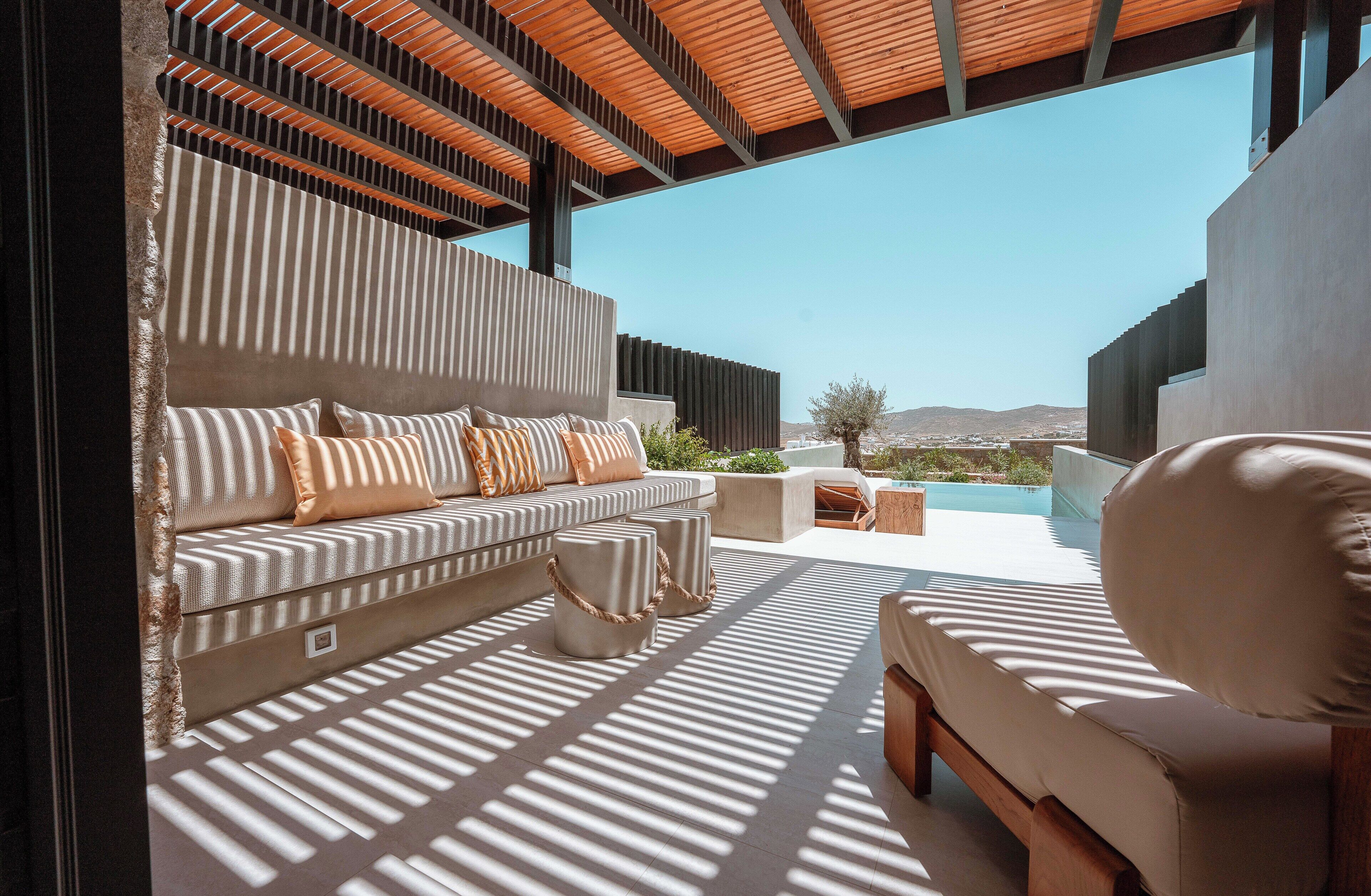 A modern outdoor seating area with a sofa and ottoman, a pool, and a view of the landscape.