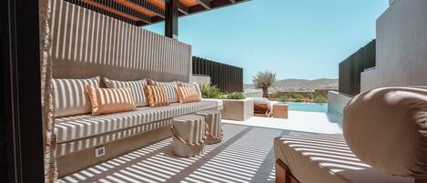 A modern outdoor seating area with a sofa and ottoman, a pool, and a view of the landscape.