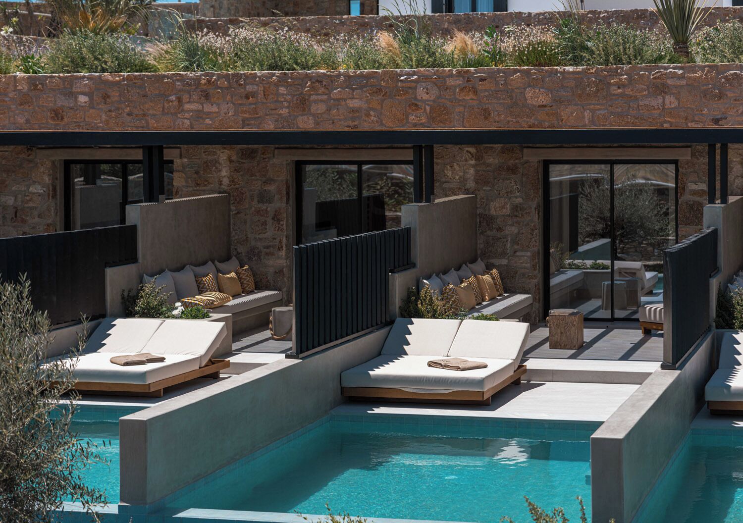 A modern outdoor pool area with built-in seating and a stone wall backdrop.