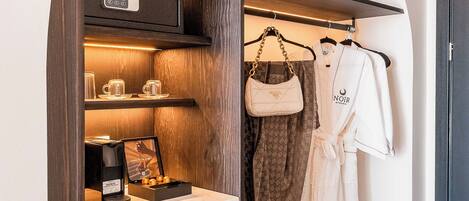 A compact, modern room with a built-in wardrobe featuring a microwave, a coffee machine, and a small seating area with a picture frame.
