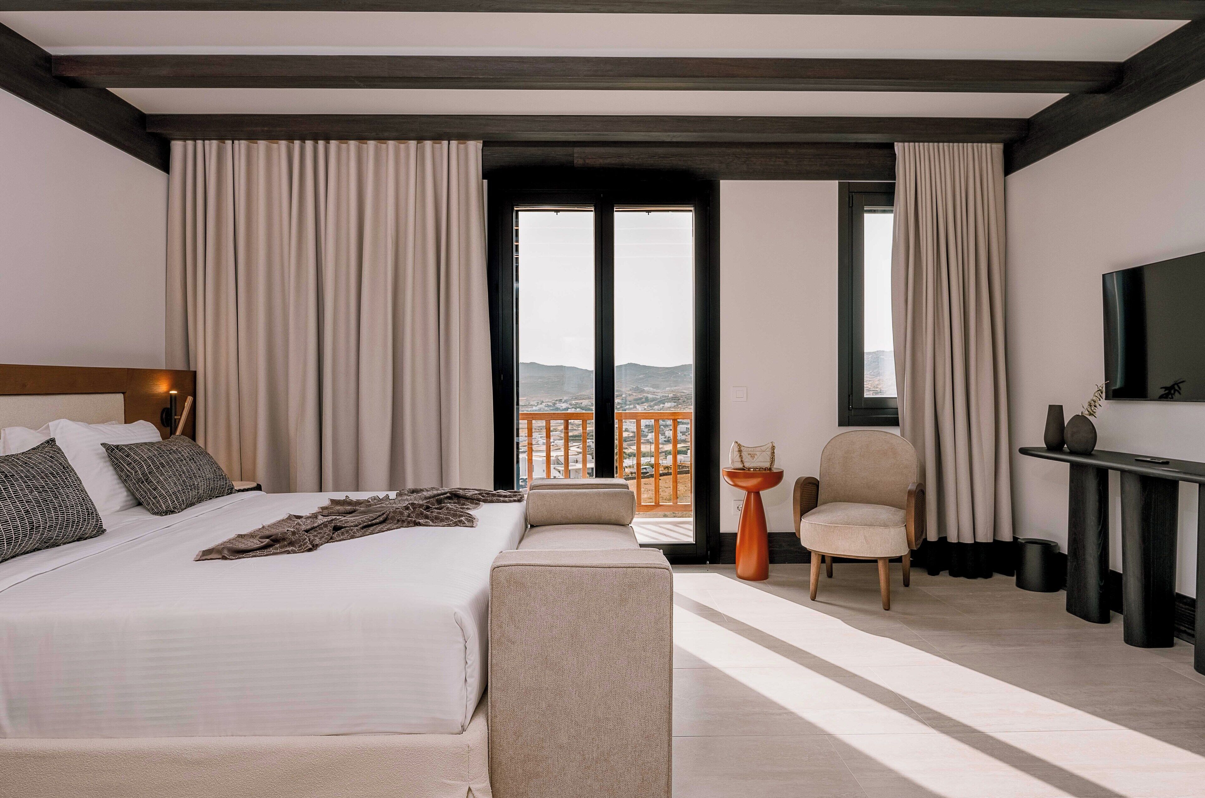 Quarto de hotel moderno com uma cama grande, um sofá, uma cadeira e uma televisão.