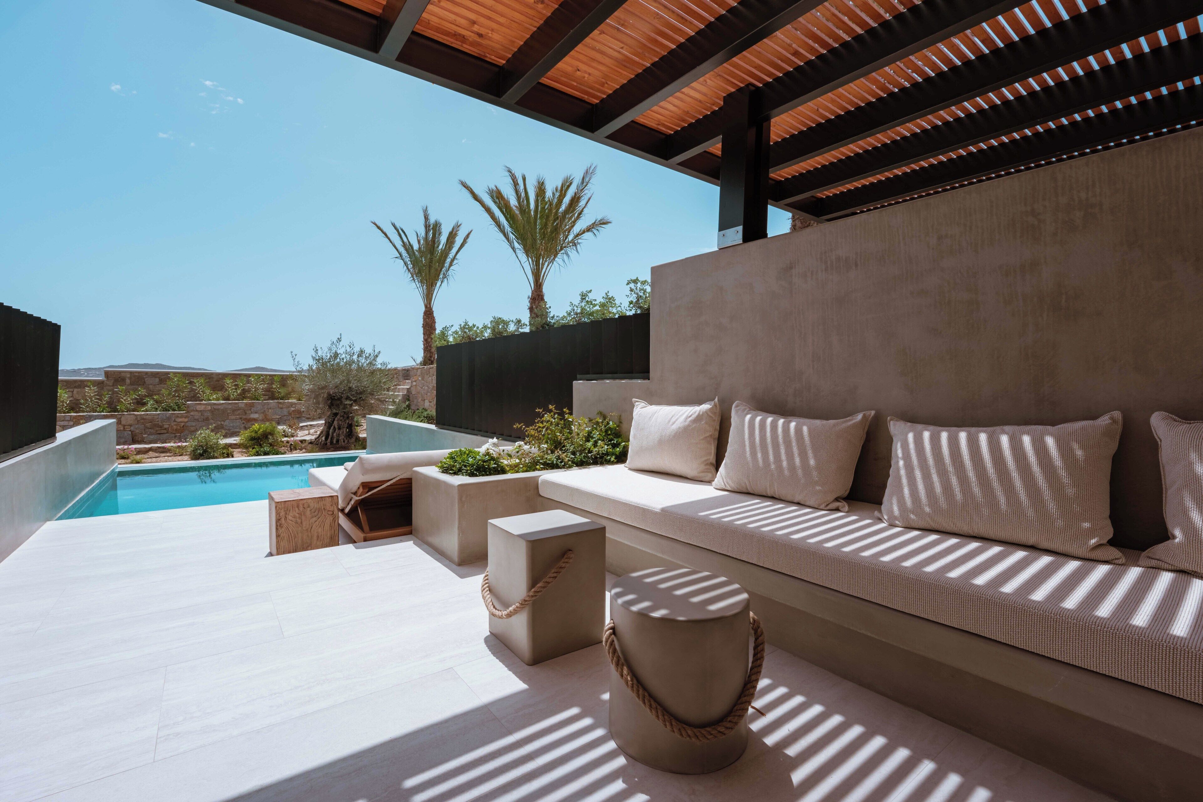 Un área de estar moderna al aire libre con piscina, techo de madera y vista a palmeras.