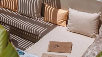 A modern outdoor seating area with a sofa and cushions, a table with a remote control, and a decorative plant.
