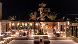 An outdoor dining area with stone walls and a central tree, surrounded by seating and tables. - Noir Mykonos (Mykonos)