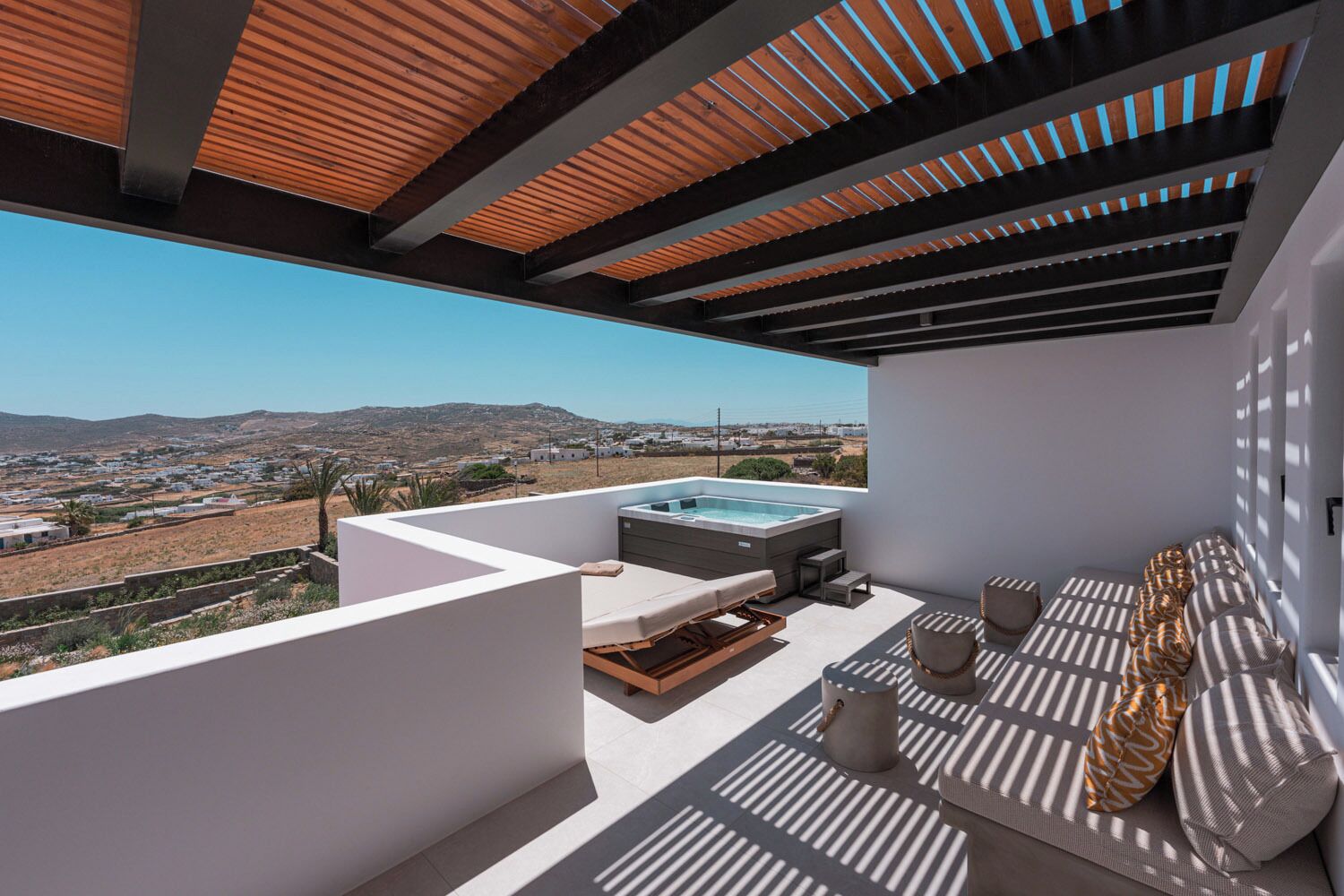 A rooftop terrace with a hot tub, seating area, and a view of a coastal landscape.