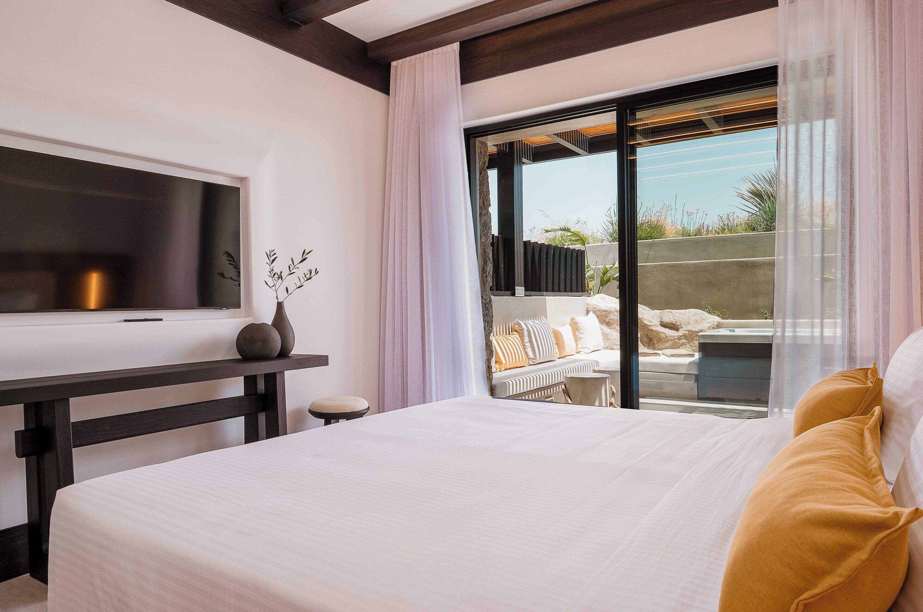 A hotel room with a bed, a TV, a desk, and a balcony with a view of the outdoors.