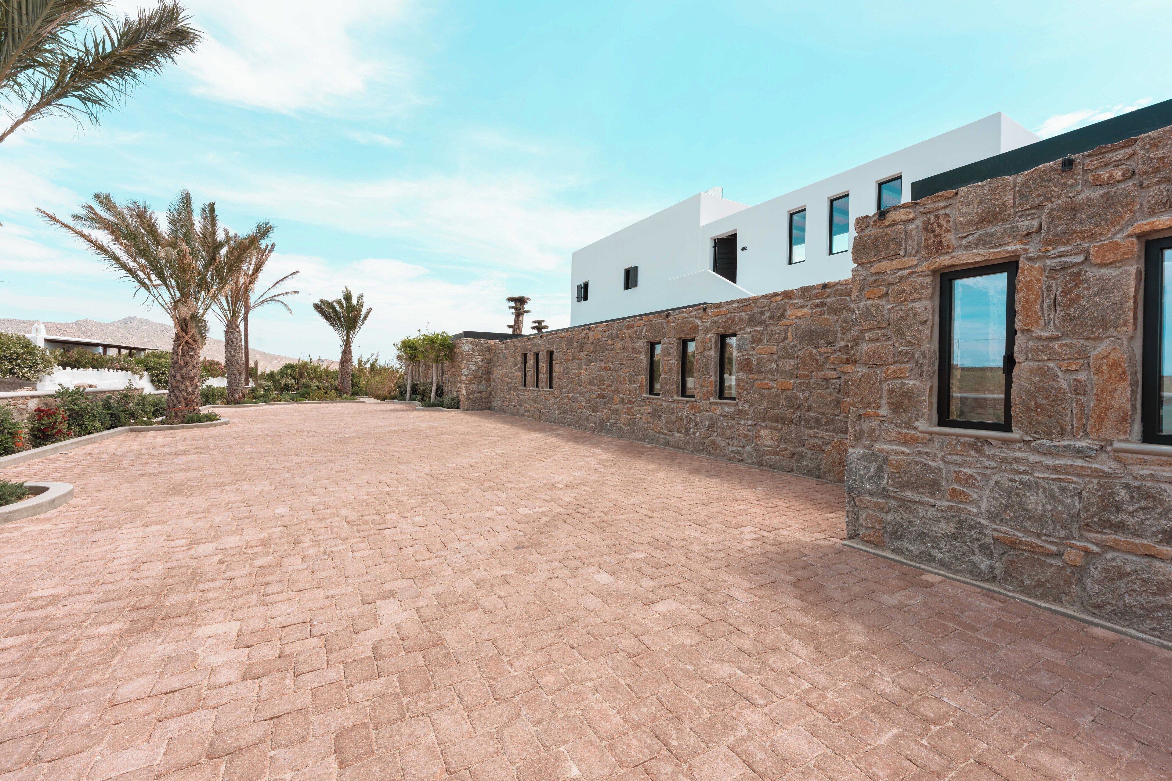 Un edificio moderno con fachada de piedra, camino pavimentado y palmeras.