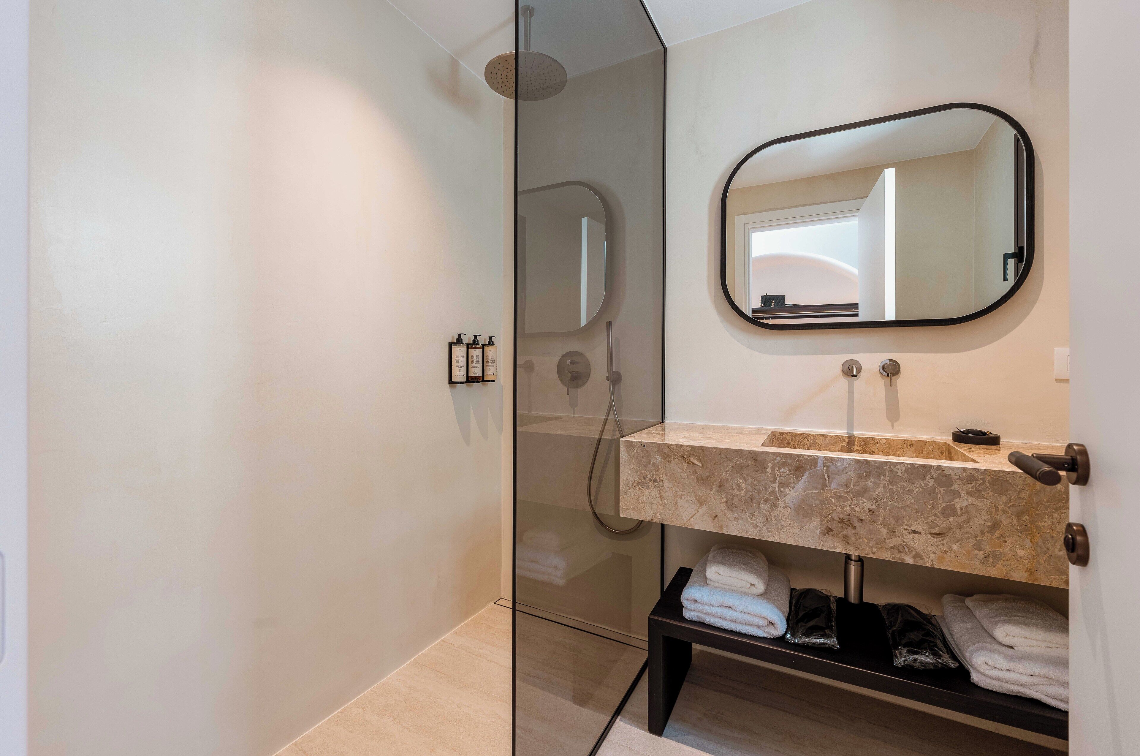 A modern bathroom with a glass-enclosed shower, a marble sink, and a black-framed mirror.