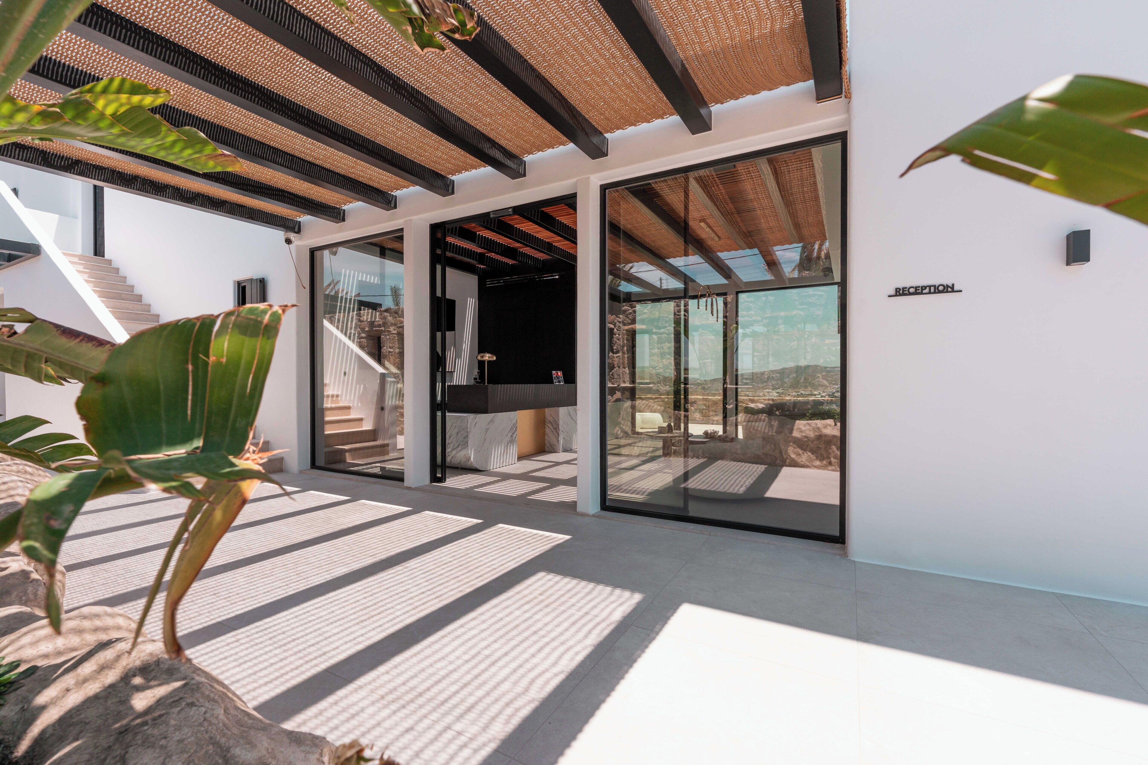 Un área de recepción moderna con un vidrio que da a un balcón, una escalera y una planta grande.