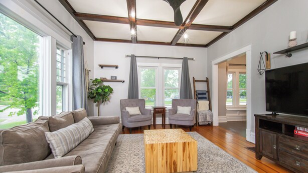 A spacious living room with a large window, a wooden coffee table, a sofa, two armchairs, and a television. - Charming 1950's Home Near Downtown, Fenced Yard, Pet Friendly! (Rapid City)