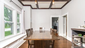A dining room with a large wooden table, chairs, and a view of the outdoors through large windows. - Charming 1950's Home Near Downtown, Fenced Yard, Pet Friendly! (Rapid City)