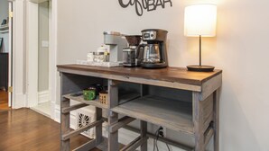 A coffee bar with a coffee maker, grinder, and a lamp on a wooden table. - Charming 1950's Home Near Downtown, Fenced Yard, Pet Friendly! (Rapid City)