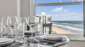 Mesa de comedor dispuesta con platos, vasos y cubiertos, con vista a una playa y al océano.