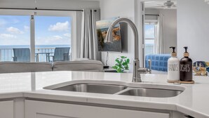 Una cocina moderna con un lavamanos grande, un ventilador de techo y vistas al océano a través de amplios ventanales.