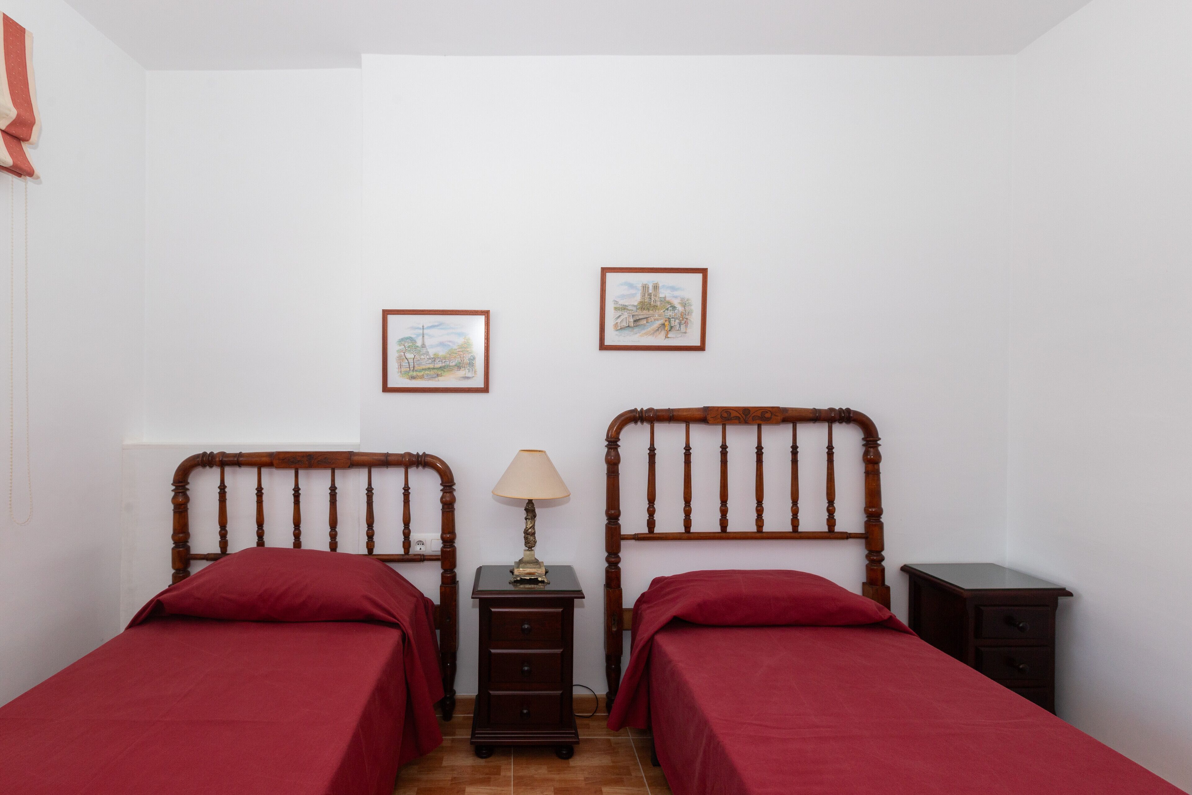 Un dormitorio con dos camas individuales, una mesita de noche con lámpara y dos cuadros enmarcados en la pared.