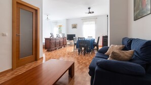 A living room with a wooden floor, a blue sofa, a wooden coffee table, and a dining area with a table and chairs. - CASA SALINAS - Apartment with mountain views and free wifi (Archidona)