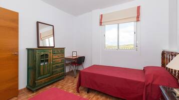 A room with two beds, a wooden cabinet, a desk with a chair, and a window with a view.