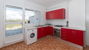 A compact kitchen with red cabinets, a washing machine, and a large window overlooking a balcony. - CASA SALINAS - Apartment with mountain views and free wifi (Archidona)