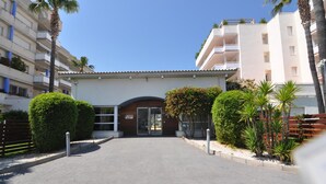 Un edificio moderno con un ingresso centrale, circondato da siepi curate e palme.