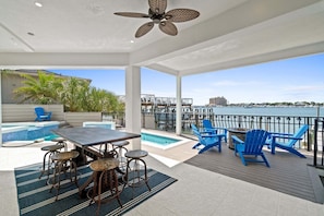A covered outdoor area with a pool, bar stools, and blue chairs.