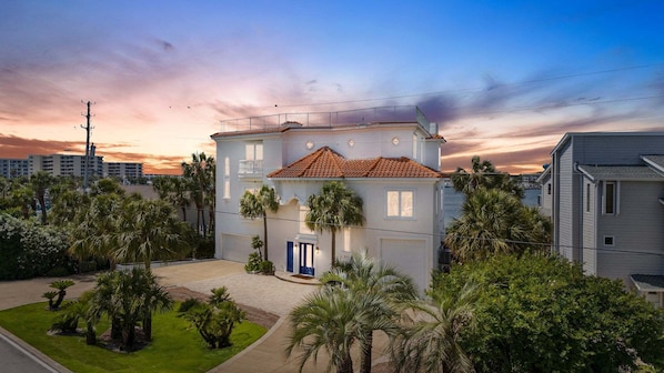 A multi-story building with a red-tiled roof, surrounded by palm trees and a clear sky.
