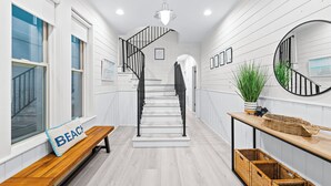 A hallway with a wooden bench, a sign reading "BEACH", a staircase with black railings, and wicker baskets on a table.