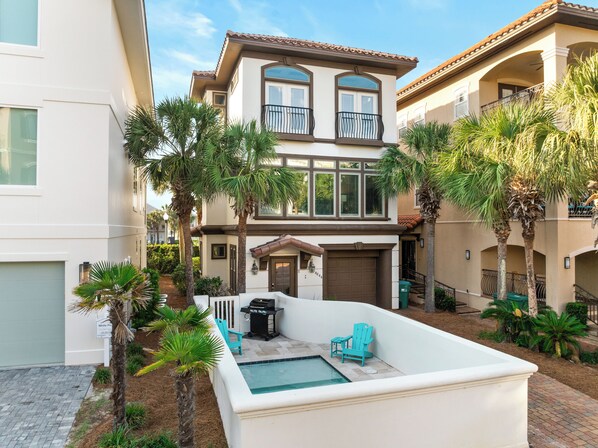 A two-story house with a pool, outdoor seating, and palm trees.
