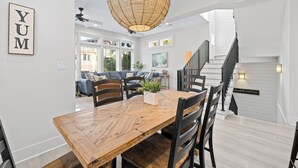 A dining area with a wooden table and chairs, a hanging light fixture, and a staircase leading to an upper level.