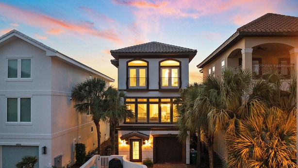 A two-story house with a swimming pool, outdoor seating, and palm trees.