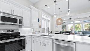 A modern kitchen with white cabinetry, stainless steel appliances, a large island with a sink, pendant lighting, and a view of the outdoors.