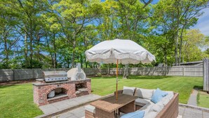 Une terrasse extérieure avec un barbecue en briques, des meubles en osier et un parasol blanc.