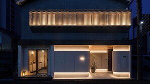 Un bâtiment moderne doté d’une grande entrée, d’un balcon avec des lames verticales et d’une plante en pot à l’intérieur.