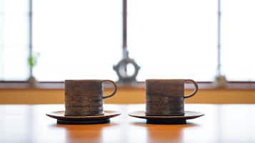Two ceramic cups on saucers on a wooden table with a window in the background.
