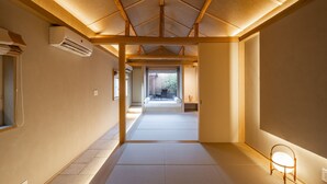 Un intérieur japonais traditionnel avec un sol recouvert de tatamis, des poutres en bois et une porte coulissante donnant sur un jardin.