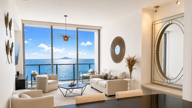 A modern living room with a large glass door leading to a balcony with a view of the sea.