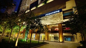 A modern hotel entrance with a well-lit facade, large columns, and a sign in a foreign language.