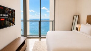 A hotel room with a large window, a bed, a TV, and a wooden bench.