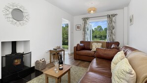 A living room with a fireplace, leather sofa, and a view of greenery outside.