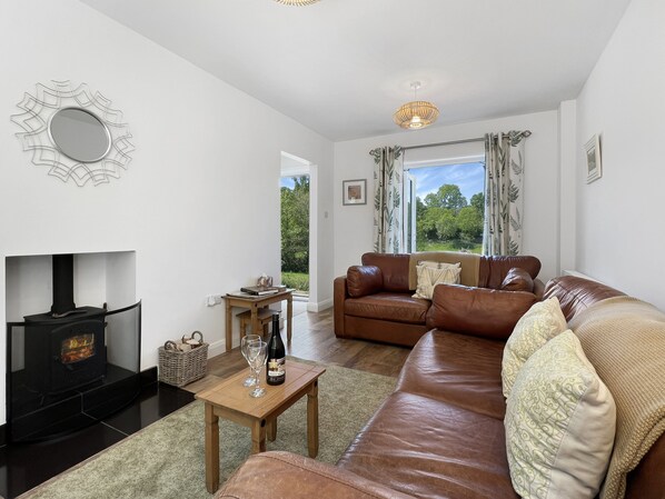 A living room with a fireplace, leather sofa, and a view of greenery outside.